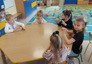 Kilkoro dzieci z grupy "Skrzatów" przy stoliku podczas poczęstunku w ramach wielkanocnego spotkania z Księdzem. Dzieci otrzymały przygotowane i udekorowane przez siebie babeczki oraz słodkie, czekoladowe jajka.