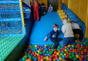 Zabawa kilku dzieci na zjeżdżalni i w basenie z piłkami w Sali Zabaw.