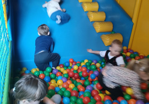 Zabawa kilku dzieci na zjeżdżalni i w basenie z piłkami w Sali Zabaw.