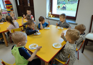 Kilkoro dzieci z grupy Pszczółek przy stoliku podczas degustacji przygotowanej przez siebie sałatki owocowej z dodatkiem miodu i soku z cytryny.