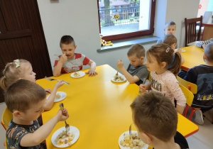 Kilkoro dzieci z grupy Pszczółek przy stoliku podczas degustacji przygotowanej przez siebie sałatki owocowej z dodatkiem miodu i soku z cytryny.