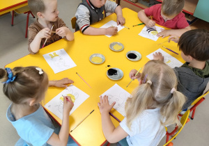 Kilkoro dzieci przy stole maluje farbą szablon pszczoły.