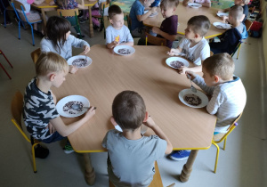 Kilkoro dzieci przy stole w trakcie śniadania-płatki czekoladowe z mlekiem.