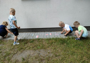 Dzieci podczas rysowania prostych obrazków kredami na chodniku.