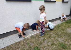 Dzieci podczas rysowania prostych obrazków kredami na chodniku.