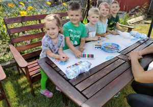 Kilkoro dzieci z Biedronek w trakcie rysowania na dużych arkuszach papieru obrazków związanych z latem i wakacjami.