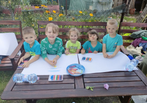 Kilkoro dzieci z Biedronek rysuje obrazki związane z wakacjami i latem na dużych arkuszach papieru.