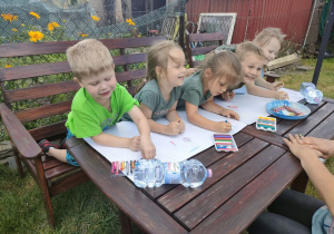 Kilkoro dzieci z Biedronek podczas rysowania obrazków związanych z latem i wakacjami na dużych arkuszach papieru.