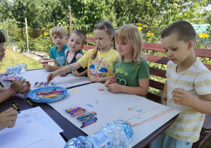 Kilkoro dzieci z Biedronek rysuje obrazki związane z latem i wakacjami na dużych arkuszach papieru.