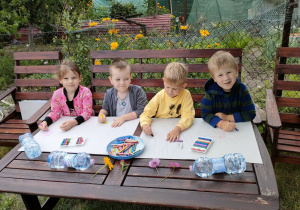 Kilkoro dzieci z Pszczółek rysuje obrazki związane z latem i wakacjami na dużych arkuszach papieru.