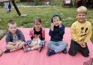 Kilkoro dzieci z Pszczółek na kocyku w trakcie głaskania królika - Baksia.