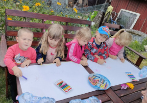 Dzieci rysują obrazki związane z latem i wakacjami za dużych arkuszach papieru.