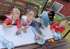 Dzieci z Pszczółek rysują obrazki związane z latem i wakacjami na dużych arkuszach papieru.