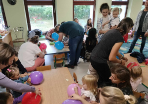 Dzieci wraz z Rodzicami ozdabiają kolorowe baloniki przy stołach.