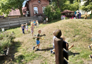 Rozgrzewka wokół górki na przedszkolnym placu zabaw wśród dzieci młodszych.
