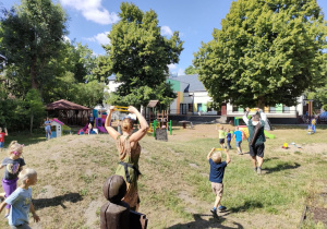 Rozgrzewka wokół górki na przedszkolnym placu zabaw wśród dzieci młodszych.