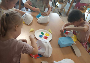 Kilkoro dzieci z grup starszych stempelkuje/maluje czapkę za pomocą gąbeczki i kolorowej farby.