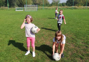 Kilkoro dzieci z grupy "Skrzatów" podczas treningu piłki nożnej na boisku sportowym.