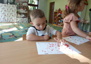 Dwoje dzieci z grupy "Żabek" przy stole maluje kropki przy wykorzystaniu swoich paluszków i kolorowej farby.