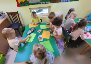 Kilkoro dzieci z grupy "Pszczółek" przy stole wykleja szablon latawca kuleczkami z kolorowej plasteliny.
