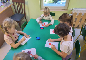 Kilkoro dzieci z grupy "Pszczółek" przy stole maluje kropki przy pomocy pędzelków i kolorowej farby.
