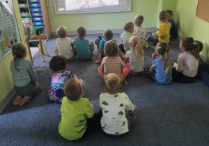Dzieci z grupy "Pszczółek" oglądają film edukacyjny o kropce na tablicy multimedialnej.