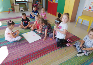 Kilkoro dzieci z grupy "Skrzatów" nakleja wycięte, kolorowe kółka na duży arkusz papieru.
