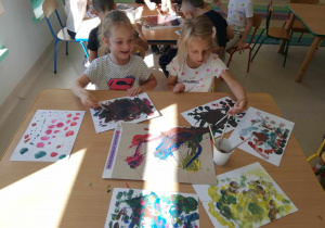 Dwie dziewczynki ze "Skrzatów" tworzą kropkowane dzieło przy wykorzystaniu pędzelków i kolorowej farby.