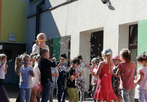 Ciocia Magda wraz z dziećmi z grupy "Skrzatów" puszcza bańki mydlane na tarasie przedszkolnym.