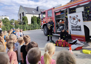Strażak prezentuje dzieciom profesjonalny sprzęt strażacki.