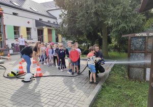 Dzieci z grupy "Skrzatów" podlewają ogródek przedszkolny, przy użyciu wody z węża strażackiego.