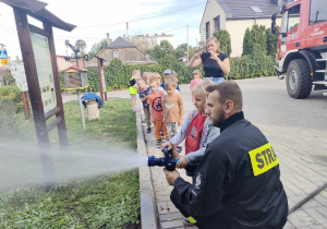 Dzieci z grupy "Biedronek" podlewają ogródek przedszkolny, przy użyciu wody z węża strażackiego.
