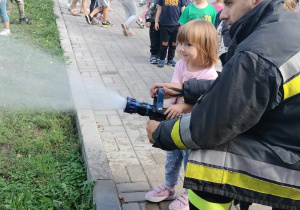 Dziewczynka z "Żabek" korzysta z węża strażackiego.