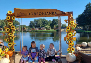 Czworo dzieci na drewnianej ławce przy pięknej scenerii Dobronianki. W tle zbiornik wodny.