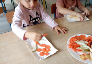 Dwoje dzieci z grupy "Żabek" przy stoliku układa coś z kawałków owoców i warzyw.