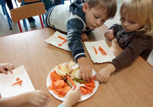 Kilkoro dzieci z grupy "Żabek" przy stoliku podczas układania oraz degustacji owoców i warzyw.