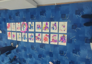 Na niebieskim dywanie leżą prace dzieci tworząc galerię prac.