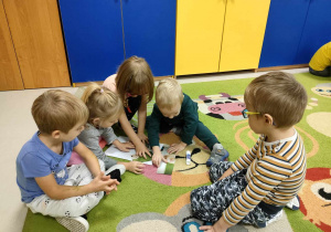 Kilkoro dzieci z grupy "Motylków" składa w całość i nakleja na kartkę ilustrację chomika.