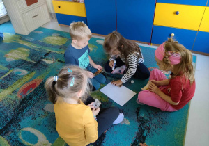 Kilkoro dzieci z "Biedronek" składa w całość i nakleja na kartkę ilustrację chomika.