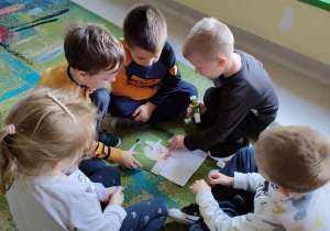 Kilkoro dzieci z "Biedronek" składa w całość i nakleja na kartkę ilustrację chomika.
