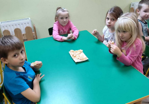Kilkoro dzieci z "Pszczółek" przy stoliku chętnie zjada jabłka.