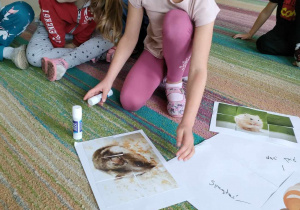 Dziewczynka ze "Skrzatów" nakleja ilustrację chomika na rogu brystolu.