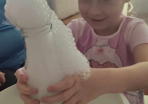 Dziewczynka z "Biedronek" trzyma w dłoni butelkę z wulkanem - ciepłą wodą, kostkami suchego lodu i mydłem w płynie.