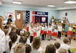 Troje dzieci z "Biedronek" wnosi Flagę Polski do sali przy akompaniamencie bębenku, na którym gra Róża.