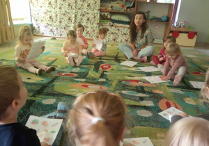 Dzieci z najmłodszej grupy siedzą na dywanie i nazywają produkty w oparciu o ilustrację.