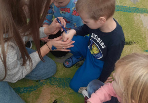 Ciocia Daria rysuje dzieciom na rączce niebieskie serduszko.