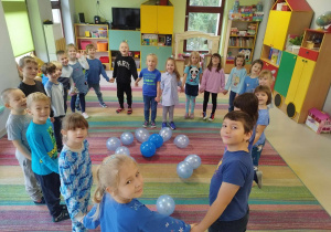 Dzieci z grupy "Skrzatów" trzymając się za ręce, utworzyły serce, pośród którego są niebieskie balony.