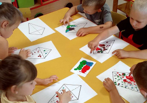 Kilkoro dzieci siedzi przy stole i maluje palcami szablon latawca.