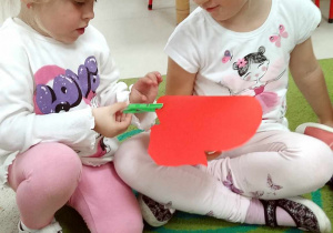 Natalia i Nikola przyczepiają spinacze do prania na papierowym jabłku.