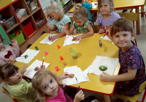 Kilkoro dzieci przy stoliku maluje kamienie za pomocą pędzelków i farby.
